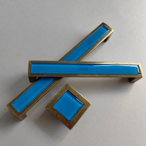 Peut inclure: Trois poignées de porte avec un insert en verre bleu et une finition en laiton. Les poignées sont en forme de rectangle et de carré.