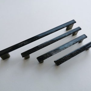 Peut inclure: Quatre poignées de porte de placard en verre noir avec une finition argentée scintillante. Les poignées sont de différentes tailles, la plus grande en haut et la plus petite en bas.