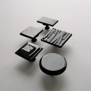 Può includere: Cinque pomelli per armadietti neri con diversi design. I pomelli sono in vetro e hanno una finitura liscia e lucida.