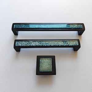 以下が含まれることがあります： 3つのキャビネット金具：2つの長方形のプルと正方形のノブ。各ピースは、黒いフレームと、質感のあるターコイズ色のガラスインサートを備えています。この金具は、引き出しやキャビネットでの使用を目的としています。
