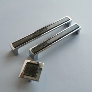 May include: Three silver cabinet pulls with black glass inserts. The pulls are rectangular and have a modern design.