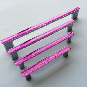 Fired glass cabinet pulls in sparkly bright pink made of fine glass sticks attached over a metal base. Slightly textured glass furniture handles with rounded edges.