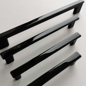 Op de afbeelding: Drie zwarte kastgrepen in verschillende lengtes. De grepen zijn gemaakt van een glad, glanzend materiaal en hebben een rechthoekige vorm.