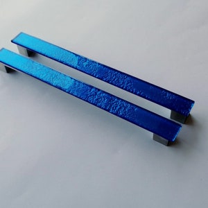 Set of two sparkly bright blue fired glass fridge pulls made of long glass sticks attached over a silvery metal base. Slightly textured glass furniture handles with rounded edges.