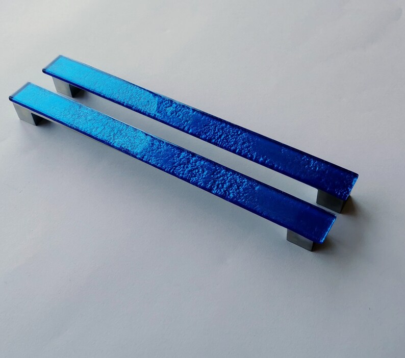 Set of two sparkly bright blue fired glass fridge pulls made of long glass sticks attached over a silvery metal base. Slightly textured glass furniture handles with rounded edges.