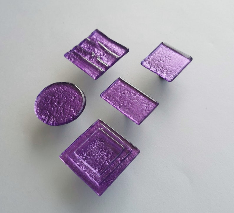 Fired glass cabinet knobs in sparkly purple made of round, square and rectangular glass pieces attached over a metal base. Slightly textured glass furniture handles with rounded edges.