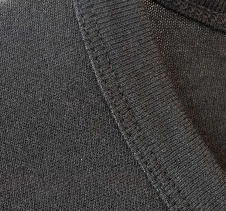May include: Close-up of a dark gray knit fabric with a stitched seam. The fabric has a textured, woven appearance.