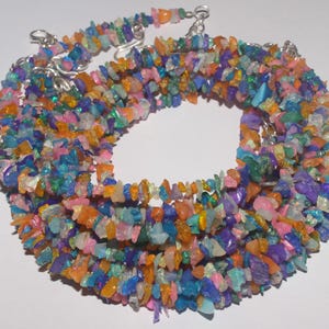 Peut inclure: Un collier à plusieurs rangs composé de petites pierres précieuses colorées de forme irrégulière. Les pierres sont un mélange d'orange, de bleu, de violet, de rose et de vert. Le collier a des fermoirs argentés.