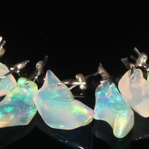 May include: A necklace featuring a series of iridescent opal gemstones. The opals display a range of colors, including blues, greens, and pinks, with a shimmering effect. Each stone is uniquely shaped and strung on a delicate silver chain, creating a beautiful jewelry piece.