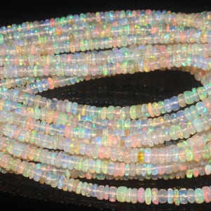 Peut inclure: Un long collier composé de petites perles d'opale circulaires et translucides. Chaque perle présente une base blanc laiteux avec des éclats irisés de lumière verte, orange et rose. Les perles sont enfilées en une ligne continue et enroulée.