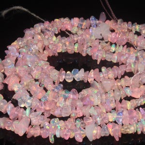 Puede incluir: Hebras de virutas de piedras preciosas de ópalo rosa. Las virutas son de forma y tamaño irregulares, con una mezcla de secciones opacas y translúcidas. Los ópalos tienen un brillo suave e iridiscente, con destellos de color.