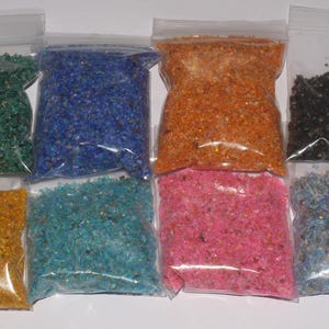 May include: Eight clear plastic bags filled with colorful crushed glass. The colors include green, blue, orange, black, yellow, turquoise, pink, and light blue. The bags are sealed with a zip closure.