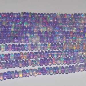 Peut inclure: Plusieurs brins de perles d'opale violettes iridescentes. Les perles sont un mélange de formes ovales et rondes, avec une qualité translucide. Les opales affichent des éclats de couleur, dont le bleu, le vert et le rose. Les perles sont enfilées, prêtes à être utilisées.