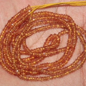 May include: Strand of small, faceted orange gemstones, likely beads, with a golden-yellow string. The beads are a warm, amber color, and appear to be strung together. The gemstones are small and uniform in size.
