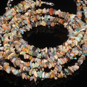 May include: A multi-strand necklace made from small, irregularly shaped opal chips in various colours, including orange, blue, green, and brown. The necklace has a silver-coloured clasp.