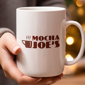 May include: White ceramic mug with a brown logo that says "MOCHA JOE'S" with a stylized coffee cup and steam coming from it.