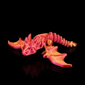 May include: A 3D-printed dragon figurine in shades of pink and orange. The dragon has detailed wings, a spiky spine, and a long tail. The figurine is set against a black background, creating a striking contrast.
