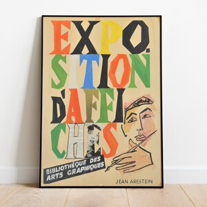 May include: A vintage poster advertising an exhibition of posters. The poster features a colourful, abstract design with the words "EXPO. SITION D'AFFICHES" in bold, colourful letters. The poster is framed in black and has the text "Bibliotheque des Arts Graphiques" and "JEAN ARESTEIN" at the bottom.