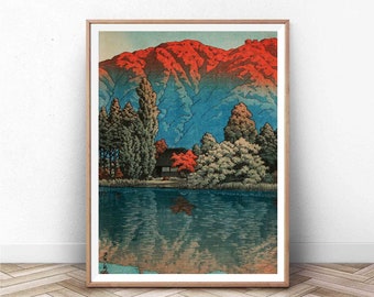 Puede incluir: Una estampa japonesa en madera que representa una cordillera de montañas con un esquema de color rojo y azul. Una pequeña casa se encuentra en la orilla de un lago con árboles en primer plano. El reflejo de las montañas y los árboles se puede ver en el agua.