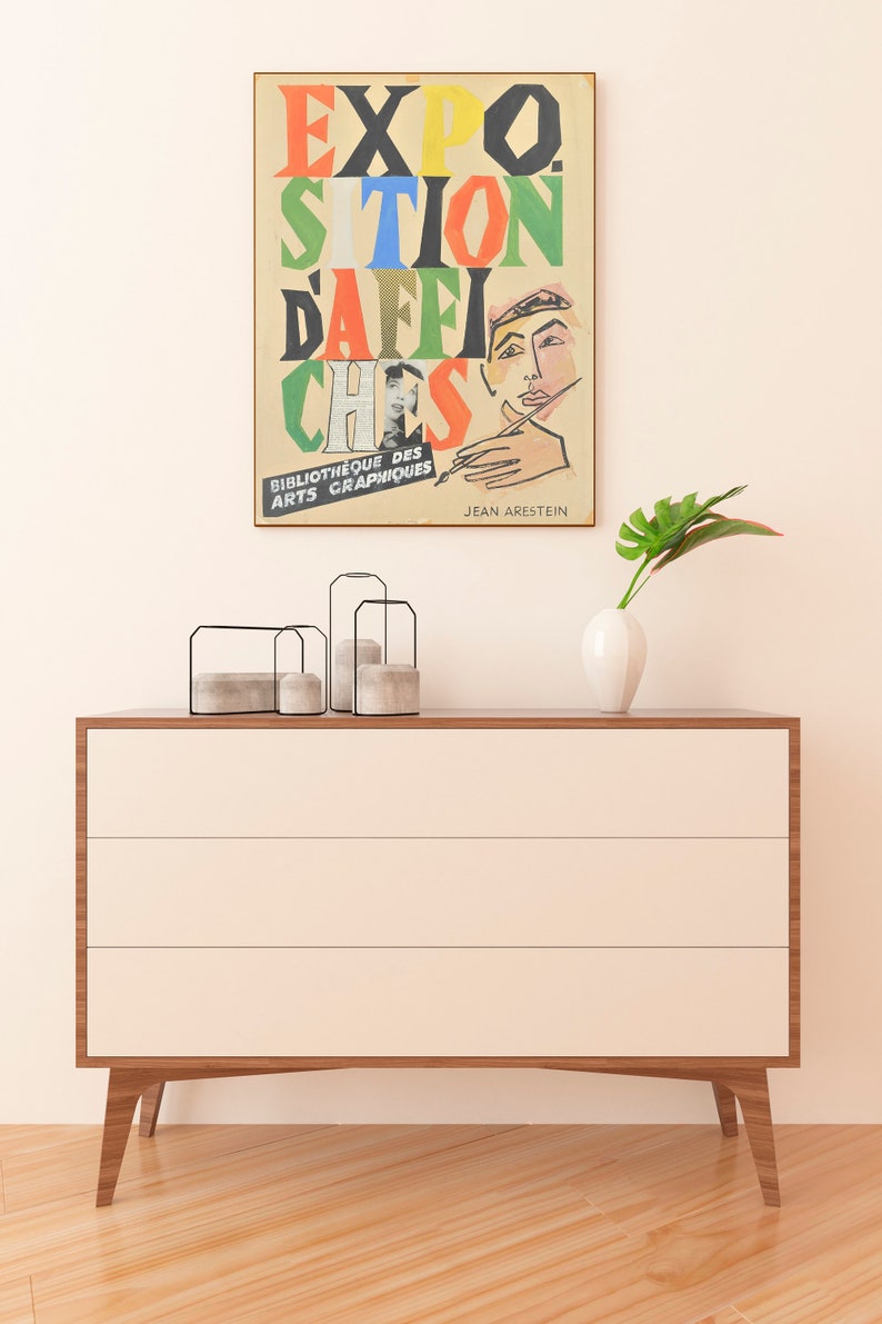 May include: A vintage poster with the text "EXPO.  SITION DAFFI CHESS" in colourful, bold letters. The poster features a drawing of a person's hand holding a paintbrush and a close-up of a person's face. The text "BIBLIOTHEQUE DES ARTS GRAPHIQUES" and "JEAN ARESTEIN" are at the bottom of the poster.