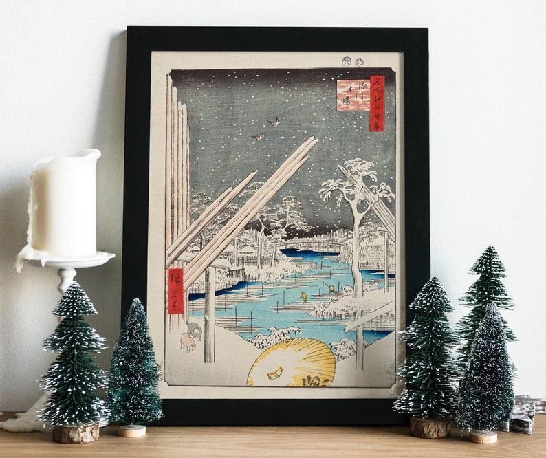 May include: A framed black and white Japanese woodblock print depicting a snowy winter scene with a river, trees, and buildings. The print is titled "Snow Scene at the River".