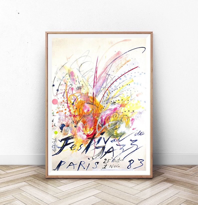 May include: A colorful abstract painting with a white background. The painting features a variety of colors, including red, orange, yellow, green, blue, and purple. The painting is framed in a wooden frame. The text "Festival de Jazz Paris 25 Oct. - 1 Nov. 83" is written in black ink at the bottom of the painting.