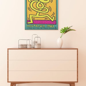 K&ouml;nnte beinhalten: Ein Vintage-Poster f&uuml;r das Montreux Jazz Festival 1983 mit einer gelben Strichm&auml;nnchenfigur, die auf einem rosa und orangefarbenen Hintergrund tanzt. Der Text auf dem Poster lautet "Montreux 1983 17&egrave;me Festival de Jazz - Juillet 24"