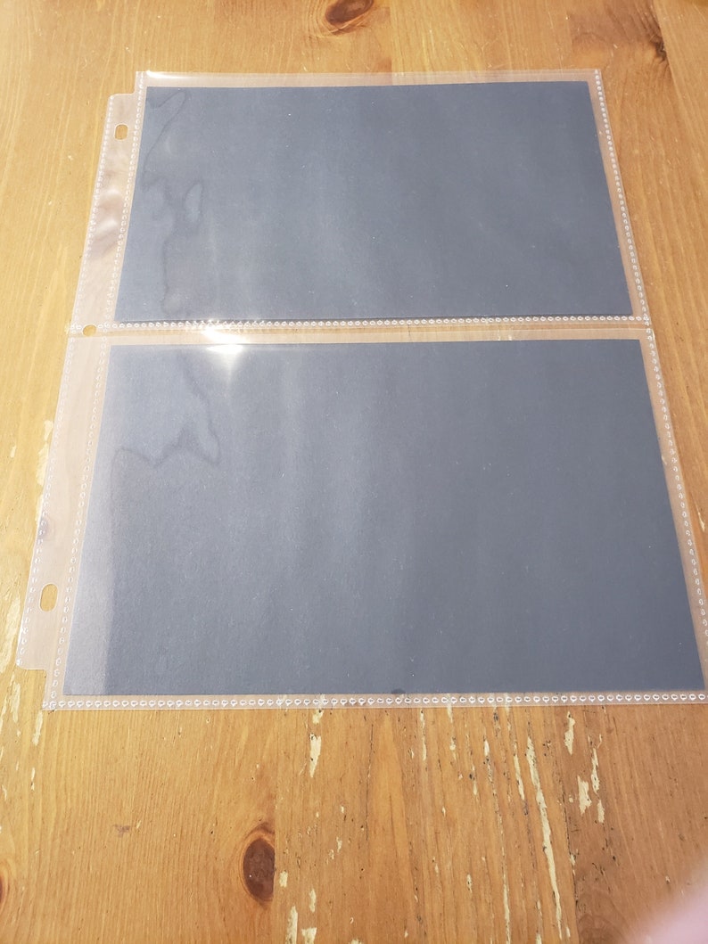 May include: Two clear plastic photo page protectors with black paper inserts. The protectors have a hole punched in the top left corner and a row of small holes along the top and bottom edges.