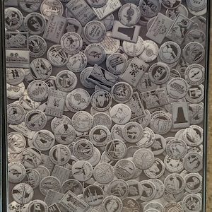 May include: A collection of round, silver-colored metal tokens with various national park and monument names and logos. The tokens are arranged in a random pattern, creating a visually interesting collage.