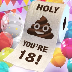 Op de afbeelding: Een rol wit toiletpapier met de woorden "HOLY YOU'RE 18!" en een lachende poep-emoji erop gedrukt. De achtergrond bevat kleurrijke ballonnen en een banner.