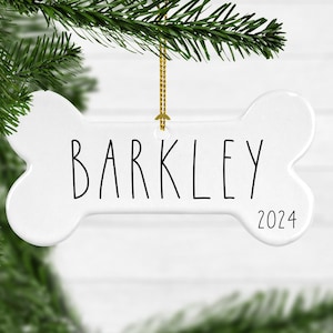 May include: White ceramic bone-shaped Christmas ornament with the name "Barkley" and the year "2024" written in black.