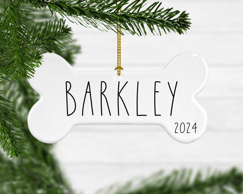 May include: White ceramic bone-shaped Christmas ornament with the name "Barkley" and the year "2024" written in black.