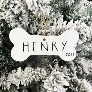 May include: White ceramic bone-shaped Christmas ornament with the name "HENRY" and the year "2022" written on it.