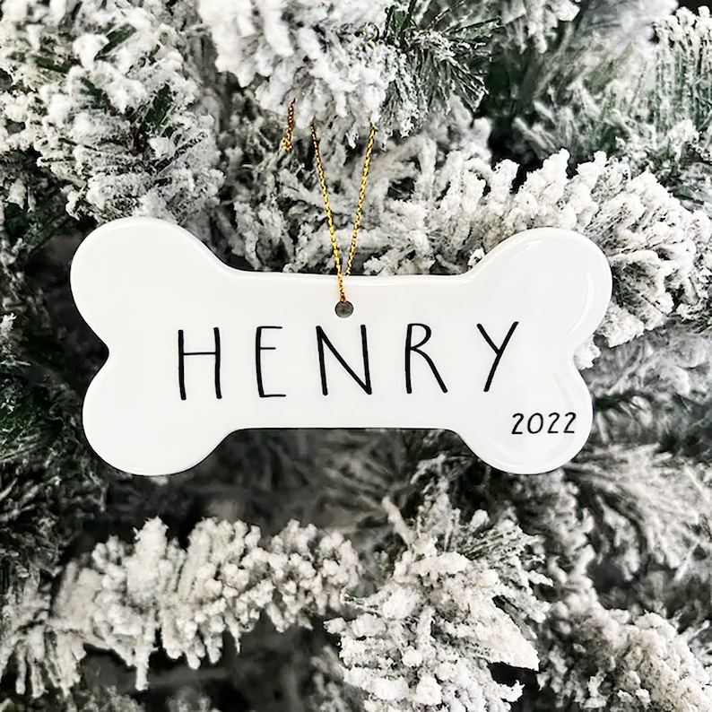May include: White ceramic bone-shaped Christmas ornament with the name "HENRY" and the year "2022" written on it.