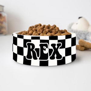 May include: A white ceramic pet bowl with a black and white checkered pattern. The word "REX" is printed in large, black, retro-style letters. The bowl is filled with brown pet food.