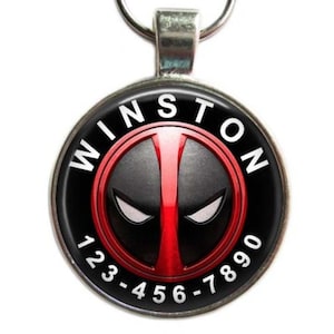 May include: A round, silver-toned pet tag with a black and red graphic design. The tag features the name "WINSTON" in white text around the edge, and a phone number below the graphic.