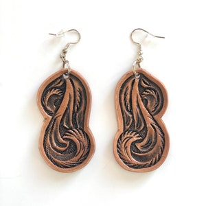 May include: A pair of brown leather earrings with a detailed floral design. The earrings are attached to silver hooks.