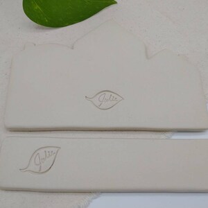 May include: Two white ceramic rectangular trays with a leaf design and the word "Julie" embossed on each.