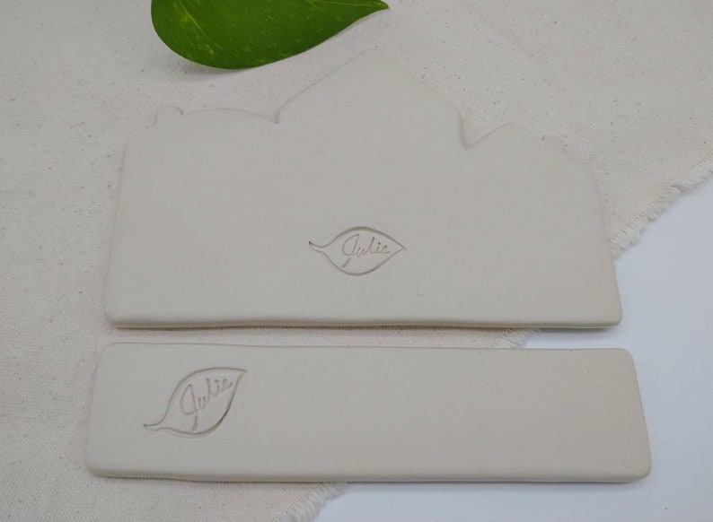 May include: Two white ceramic rectangular trays with a leaf design and the word "Julie" embossed on each.