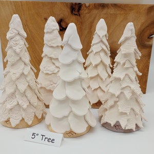 Op de afbeelding: Vijf witte keramische kerstboompjes, elk met een unieke textuur, staan op een houten oppervlak. De boompjes zijn 12,7 cm hoog en hebben een rustieke, handgemaakte uitstraling. "5" Tree staat op een bordje voor de boompjes.