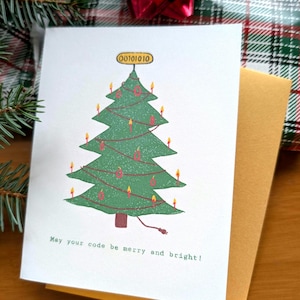 以下が含まれることがあります： 緑色のクリスマスツリー、赤いオーナメント、灯ったキャンドル、バイナリコード00101010が書かれた黄色いツリートップ、電源コードが描かれた白いグリーティングカード。テキストには「May your code be merry and bright!」と書かれています。