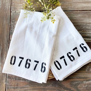 May include: Two white kitchen towels with black stenciled numbers. The towels have the numbers 07676 on them.