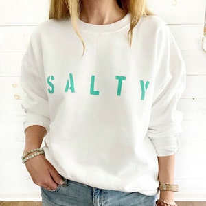 May include: White sweatshirt with the word "SALTY" printed in teal green letters.