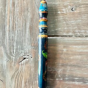 May include: A hand-painted wooden pencil with a white tip. The pencil is dark blue with colorful floral and leaf designs. The top is decorated with blue, orange, and yellow patterns. The pencil is approximately 8 inches long.