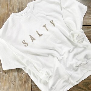 May include: White sweatshirt with the word "SALTY" printed in brown on the front.