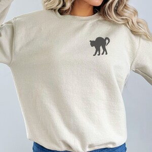 Op de afbeelding: Een lichtbeige sweatshirt met een zwart silhouet van een kat op de voorkant.
