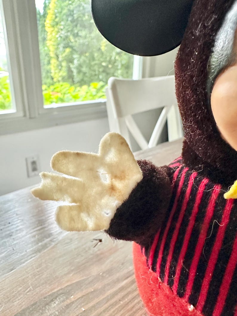 May include: Vintage Mickey Mouse plush toy. The plush features a red and black striped shirt, a black head, and a cream-colored felt hand. The toy has a yellow bow tie and a red body.