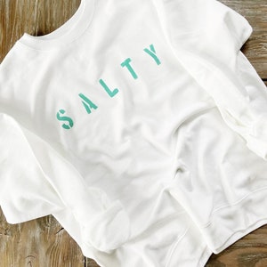 May include: White sweatshirt with the word "SALTY" printed in teal green.
