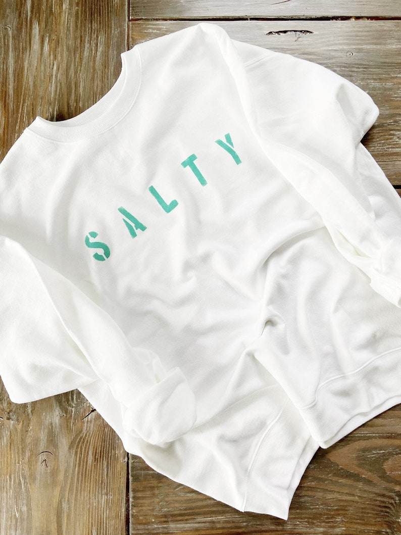 May include: White sweatshirt with the word "SALTY" printed in teal green.