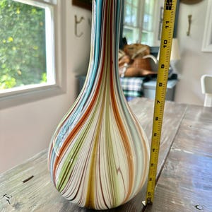 K&ouml;nnte beinhalten: Eine hohe, tropfenf&ouml;rmige Glasvase mit bunten vertikalen Streifen in Blau-, Orange-, Gr&uuml;n- und Braunt&ouml;nen. Die Vase ist etwa 28 cm hoch. Dekorative Heimdekoration.